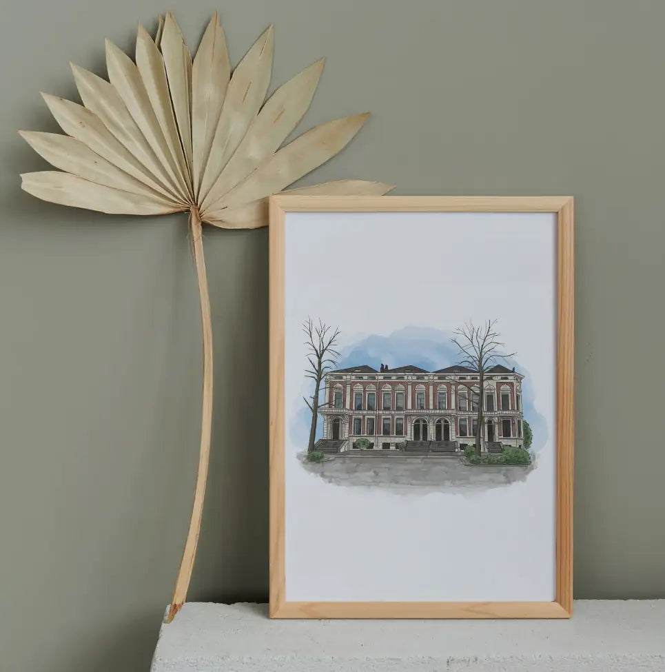 Ingelijste illustratie van historisch gebouw naast gedroogd palmblad decor.